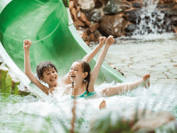 Twee kinderen komen uit de waterglijbaan gezwaaid. 