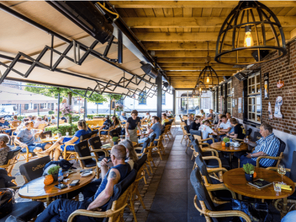 Volle terras met mensen, veel drankjes en eten, gezelligheid is aanwezig.
