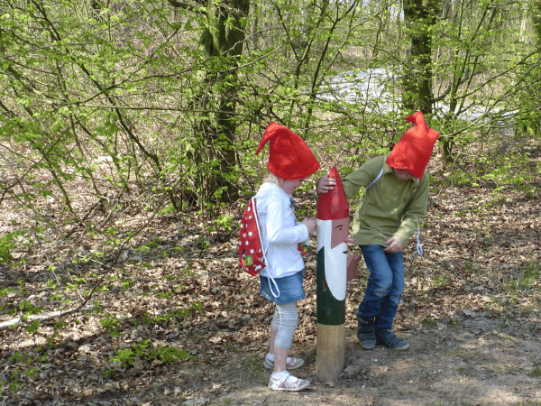 Kinderen met rode mutsjes staan naast een kabouter paaltje.