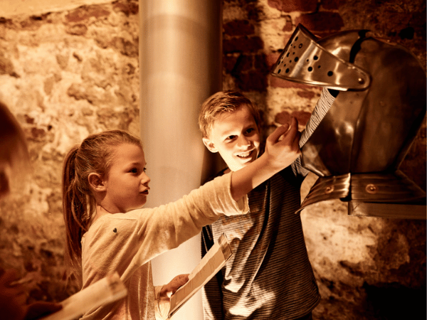 Kinderen bekijken de gevechtshelm van de ridder. 