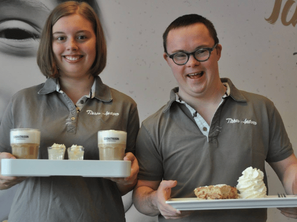 Een jongen en een meisje staan met een kop koffie en gebakje.